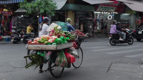 Una-Mujer-Vendiendo-Frutas-Frescas-Desde-Su-Bicicleta-En-Una-Concurrida-Calle-De-Hanoi,-Vietnam,-Con-Colores-Vibrantes-Y-Actividad-Bulliciosa.