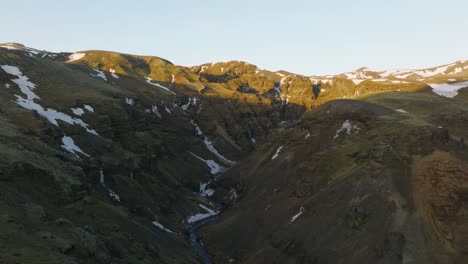 Aerial-landscape-view-over-a-mountain-valley-with-a-river-flowing-and-snow-melting