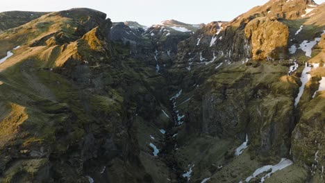 Aerial-landscape-view-of-a-mountain-canyon-with-a-river-flowing-from-melting-snow,-on-a-sunny-morning-in-Iceland