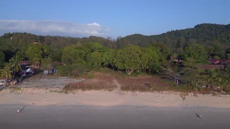 Los-Turistas-Disfrutan-De-Caminar-Por-La-Playa-Al-Atardecer-Con-Un-Exuberante-Bosque-Tropical-Verde-En-El-Fondo