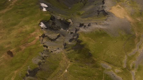 Aerial-footage-showcasing-the-rugged-and-diverse-terrain-around-Sólheimajökull-Glacier-in-Iceland,-highlighting-the-contrast-between-rocky-outcrops-and-green-fields