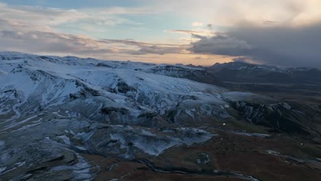 Stunning-aerial-footage-of-the-snow-covered-mountains-in-Myrdalur,-Iceland,-during-a-picturesque-sunset