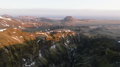 Aerial-panoramic-view-over-a-mountain-canyon-with-a-river-flowing-from-melting-snow,-in-Iceland,-on-a-sunny-morning