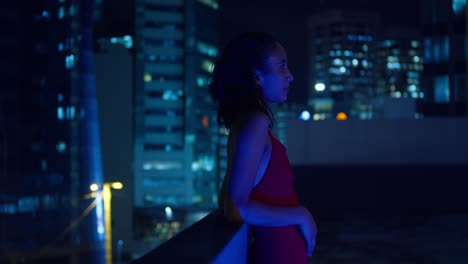 On-a-rooftop,-a-Hispanic-girl-stands-with-Port-of-Spain,-Trinidad's-Caribbean-city-lights-in-the-background