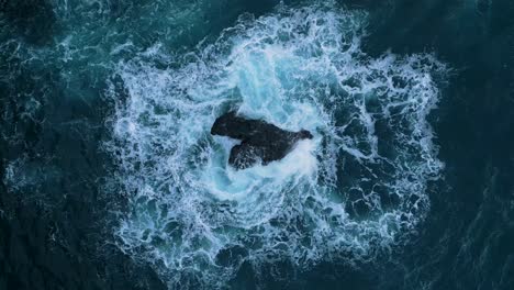 Aerial-drone-footage-of-the-sea,-showing-waves-flowing-around-a-rock