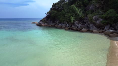 Turquoise-ocean-water-meeting-a-rocky-shore-with-a-lush-green-jungle-forest-on-a-tropical-island