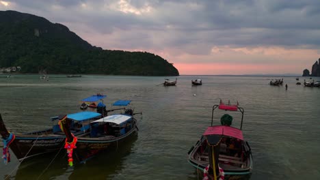 Traditionelle-Thailändische-Longtail-Boote,-Die-Bei-Sonnenuntergang-Auf-Ruhigem-Wasser-Schwimmen,-Mit-Dramatischem-Himmel-Im-Hintergrund,-Überflugdrohne