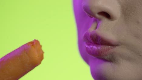 woman-taking-a-bite-from-carrot-in-close-up,-neon-color-background