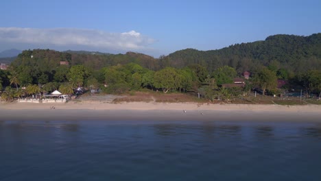 Tourists-enjoying-walking-on-the-beach-at-sunset-with-lush-green-tropical-forest-in-the-background