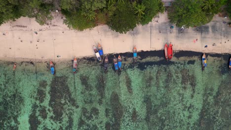 Colorful-boats-moored-at-a-tropical-island-beach,-with-tourists-walking-on-the-white-sand