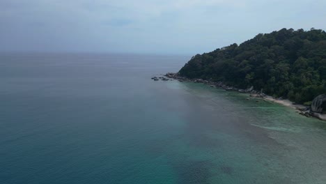 Turquoise-water-gently-washing-a-sandy-beach-surrounded-by-granite-rocks-and-lush-tropical-vegetation