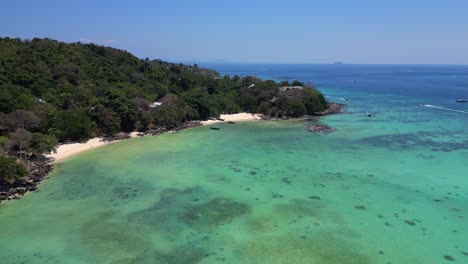 Luftaufnahme-Eines-Tropischen-Inselstrandes-Mit-Türkisfarbenem-Wasser,-Auf-Dem-Longtail-Boote-Warten,-Die-In-Thailand-Auf-Touristen-Warten