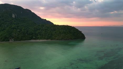 Herrlicher-Luftblickflug-über-Eine-Tropische-Insel-Bei-Sonnenuntergang-Und-Wolkigem-Himmel-Mit-Booten,-Die-Auf-Einem-Türkisfarbenen-Meer-Segeln