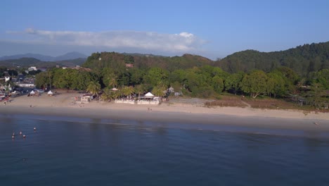 Tourists-enjoying-walking-on-the-beach-at-sunset-with-lush-green-tropical-forest-in-the-background