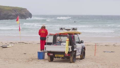 RNLI-lifeguard-in-red-clothes-next-to-beach-patrol-truck-keeps-an-eye-on-surfers