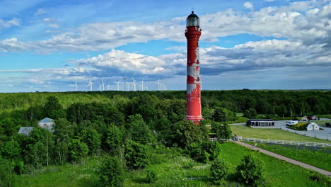 Pakri-lighthouse-surrounded-by-lush-greenery-and-wind-turbines-under-a-blue-sky,-aerial-view