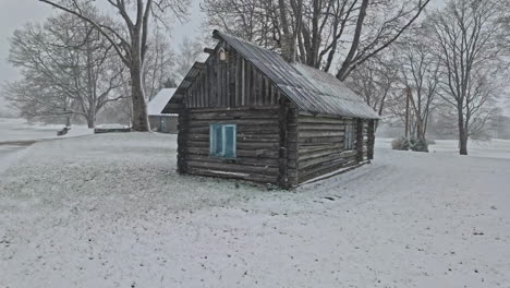 Cabaña-De-Madera-En-Invierno,-Hierba-Cubierta-De-Nieve,-Nevando-En-El-Bosque