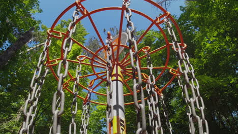 A-close-up-view-of-a-disc-hitting-the-chains-of-a-disc-golf-basket-under-a-bright-blue-sky,-capturing-the-moment-of-scoring-in-a-wooded-area