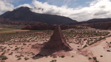 Drone-footage-of-the-natural-Obelisco-in-Quebrada-de-las-Conchas,-Salta-Argentina,-a-mountain-in-the-horizon-and-clouds