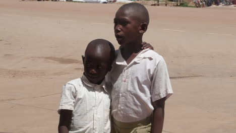 Two-young-boys-in-white-shirts-stand-close-on-a-sunny-day-in-Kampala-Uganda,-hugging-each-other