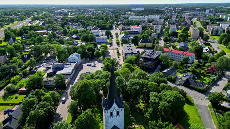 Keila-church-surrounded-by-lush-green-trees-and-residential-buildings,-aerial-view