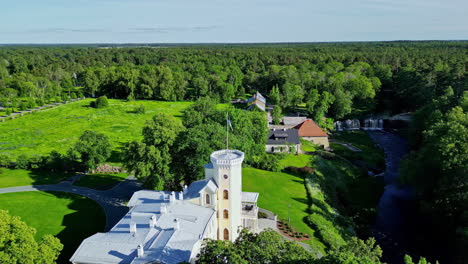 Keila-waterfall-and-a-nearby-historic-building-surrounded-by-lush-greenery,-aerial-view