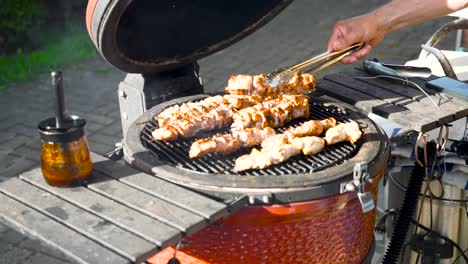 Handheld-footage-of-chicken-being-barbecued-and-grilled-on-a-red-grill-during-the-day-and-summer-time-in-Estonia,-Europe-shot-in-4K