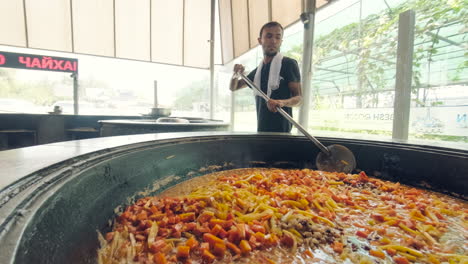 Chef-preparing-in-massive-cauldron-Plov-typical-food,-Uzbekistan