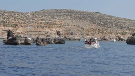 A-picturesque-view-of-Malta's-coastline,-with-boats-docked-near-the-shore-and-islands-featuring-sparse-vegetation-under-a-sunny-sky,-showcasing-natural-beauty-and-tranquility