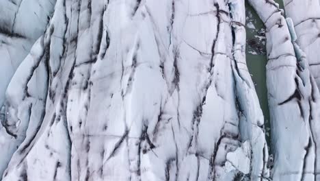 A-top-down-tilt-up-drone-flight-over-a-glacier-in-Iceland-reveals-a-scenic-panorama-overlooking-a-fjord,-tundra,-and-a-cloudy-sky-on-the-horizon