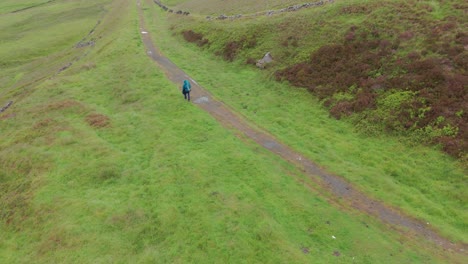 Moving-aerial-view-of-an-alone-tourist-trekking-up-the-Peak-district-National-Park-in-Derbyshire,-England