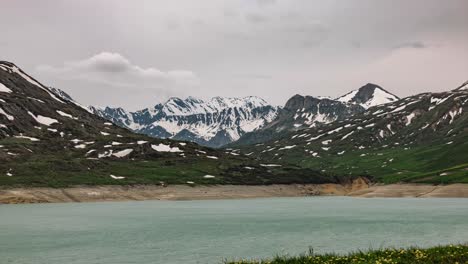 Timelapse-view-of-serene-Mont-Cenis-landscape-showing-snow-capped-peaks,-lush-green-valleys,-and-a-calm-turquoise-lake-under-a-cloudy-sky,-perfectly-capturing-the-beauty-of-nature