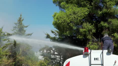 Slow-motion-footage-of-municipality-crew-of-Kifissia,-Greece,-spraying-pine-trees-with-pressurised-water-,-to-prevent-spreading-of-fire