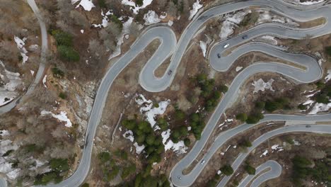 Aerial-Birds-Eye-View-captures-a-scenic-winding-mountain-road-amidst-a-forest-landscape,-with-patches-of-snow-visible