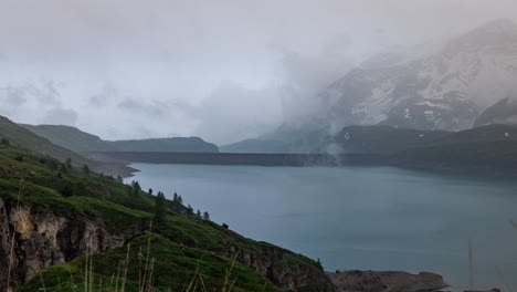 Zeitrafferansicht-Der-Ruhigen-Landschaft-Des-Mont-Cenis-Mit-Schneebedeckten-Gipfeln-Und-Einem-Ruhigen-Türkisfarbenen-See-Unter-Einem-Nebligen,-Wolkigen-Himmel,-Der-Die-Schönheit-Der-Natur-Perfekt-Einfängt