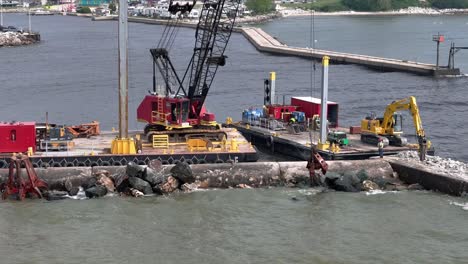 Using-a-grapple,-a-crane-moves-pieces-of-riprap-to-build-up-a-pier-in-Algoma,-WI-on-Lake-Michigan