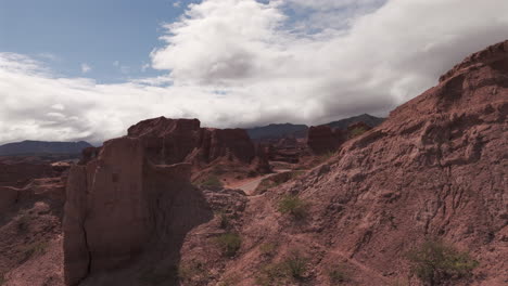 Drone-moves-forward-passing-near-the-rock-formations-while-a-truck-goes-along-the-road-next-to-Las-Ventanas-in-La-quebrada-de-las-conchas,-Salta,-Argentina