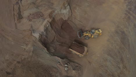 Excavator-filling-dump-truck-at-nickel-mine-site,-Western-Australia,-aerial-top-down-shot