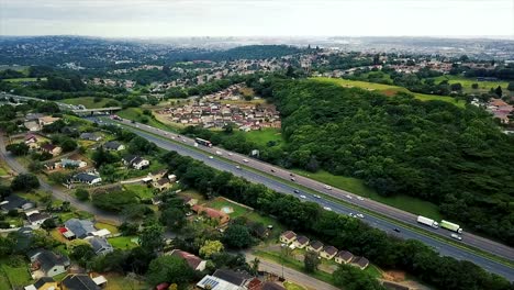 Luftaufnahmen-Einer-Drohne,-Die-über-Wohnhäuser-Mit-Blick-Auf-Eine-Viel-Befahrene-Autobahn-Mit-Fließendem-Verkehr-In-Einem-Vorort-Von-Yellow-Wood-Park-Durban-Fliegt