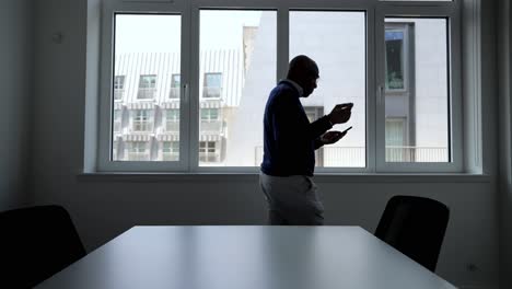 Black-man-pacing-in-a-modern-meeting-room-while-using-a-smartphone