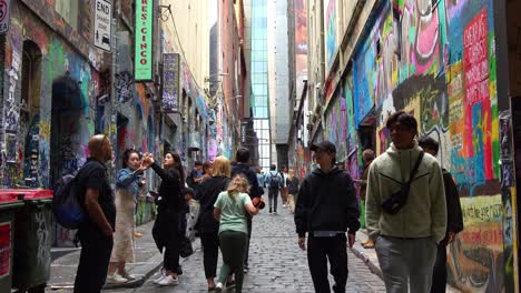 Tourists-walking-through-Hosier-Lane-in-Melbourne-city,-a-popular-cobblestone-laneway-with-a-vibrant-array-of-art-murals-and-graffiti-on-the-walls,-a-creative-cultural-street-scene