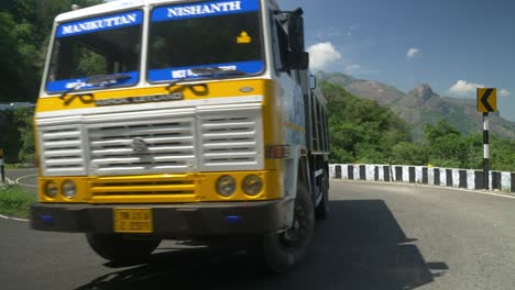 Vehicles-driving-through-a-winding-mountain-road-with-caution-signs-indicating-a-curve,-Hair-pin-bend-road-go-slow-red-sign-board