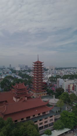 Vertical-video-of-Buddhist-Pagoda-in-Ho-Chi-Minh-City,-Vietnam-with-prayer-tower-and-red-roof-situated-in-densely-populated-area-of-the-city