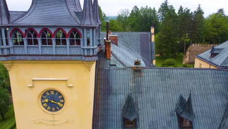 Aerial-view-of-the-clock-tower-and-rooftops-of-Zruc-nad-Sazavou-Castle-in-the-Czech-Republic,-surrounded-by-greenery