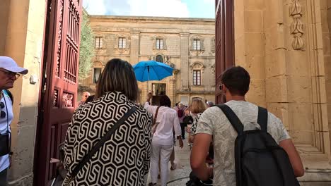 Travelers-and-visitors-enter-through-the-doors-of-a-popular-tourist-spot-in-Mdina,-Malta,-embodying-the-charm-of-historical-exploration-and-cultural-discovery