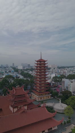 Vertical-video-of-Buddhist-Pagoda-in-Ho-Chi-Minh-City,-Vietnam-with-prayer-tower-and-red-roof-situated-in-densely-populated-area-of-the-city