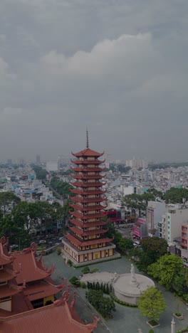 Vertical-video-of-Buddhist-Pagoda-in-Ho-Chi-Minh-City,-Vietnam-with-prayer-tower-and-red-roof-situated-in-densely-populated-area-of-the-city