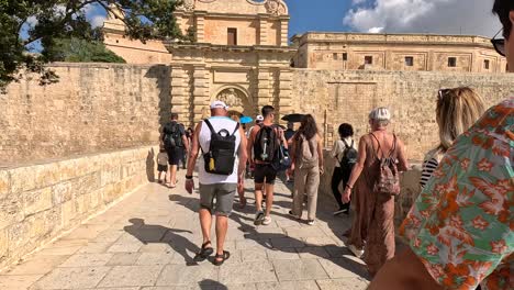 Travelers-and-visitors-stroll-across-a-bridge-near-Mdina's-historic-buildings-on-a-sunny-day,-capturing-the-essence-of-architectural-heritage-and-tourism-in-Malta