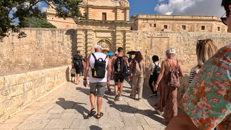 Viajeros-Y-Visitantes-Cruzan-Un-Puente-Cerca-De-Los-Edificios-Históricos-De-Mdina-En-Un-Día-Soleado,-Capturando-La-Esencia-Del-Patrimonio-Arquitectónico-Y-El-Turismo-En-Malta.