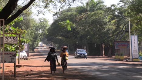 Mujer-Africana-En-Una-Calle-Muy-Transitada,-Llevando-Cestas-En-La-Cabeza-Mientras-Camina-Casualmente